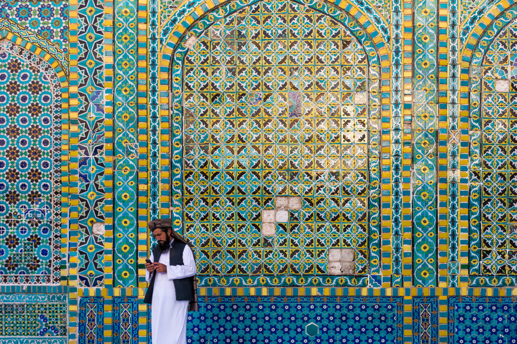 Photos of Mazar-i-Sharif, Afghanistan - Man checking phone in front of the mosaic walls of the Blue Mosque - Lost With Purpose