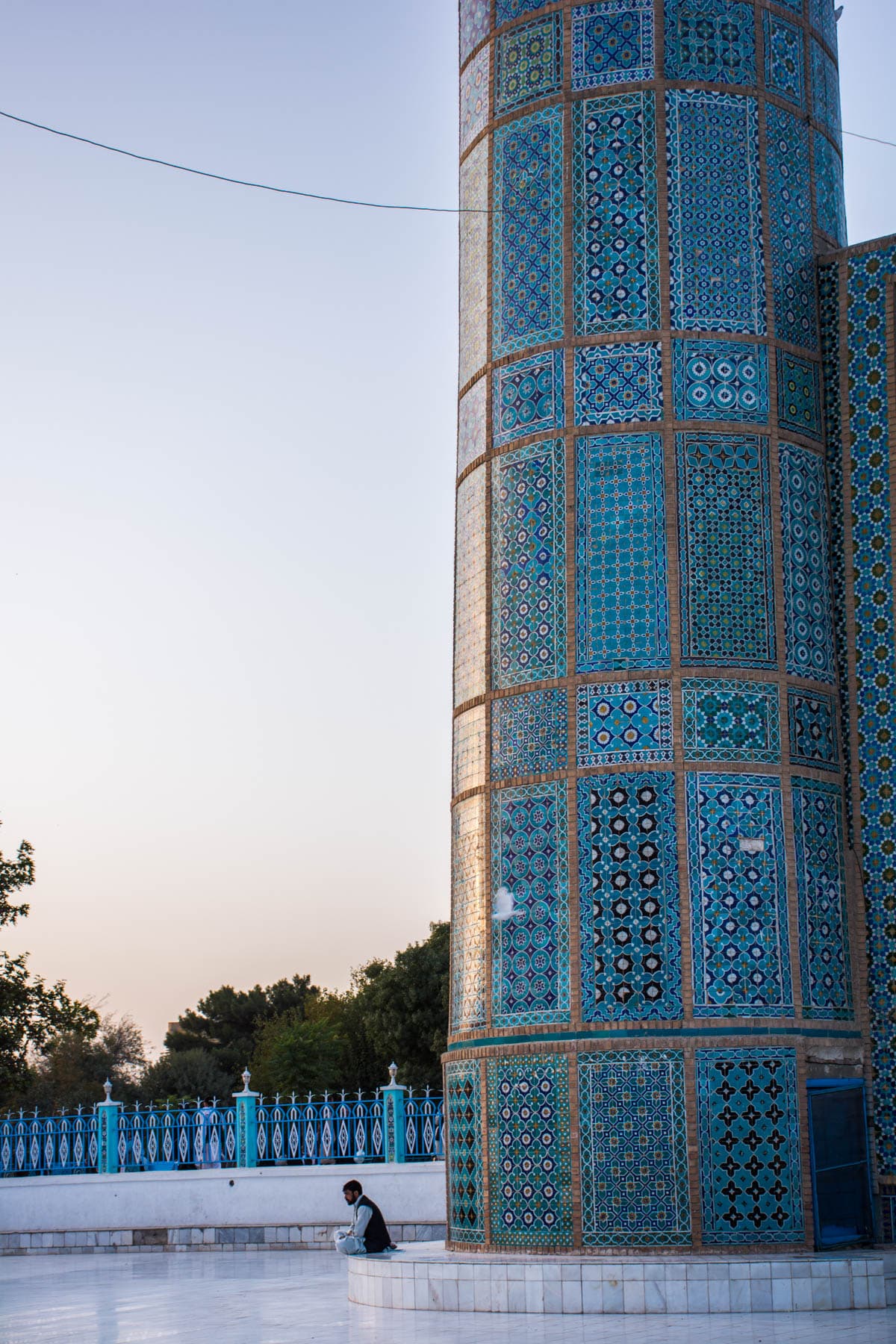 A man sitting contemplatively at the foot of a minaret of the Blue Mosque in Mazar-i-Sharif, Afghanistan, at sunset.