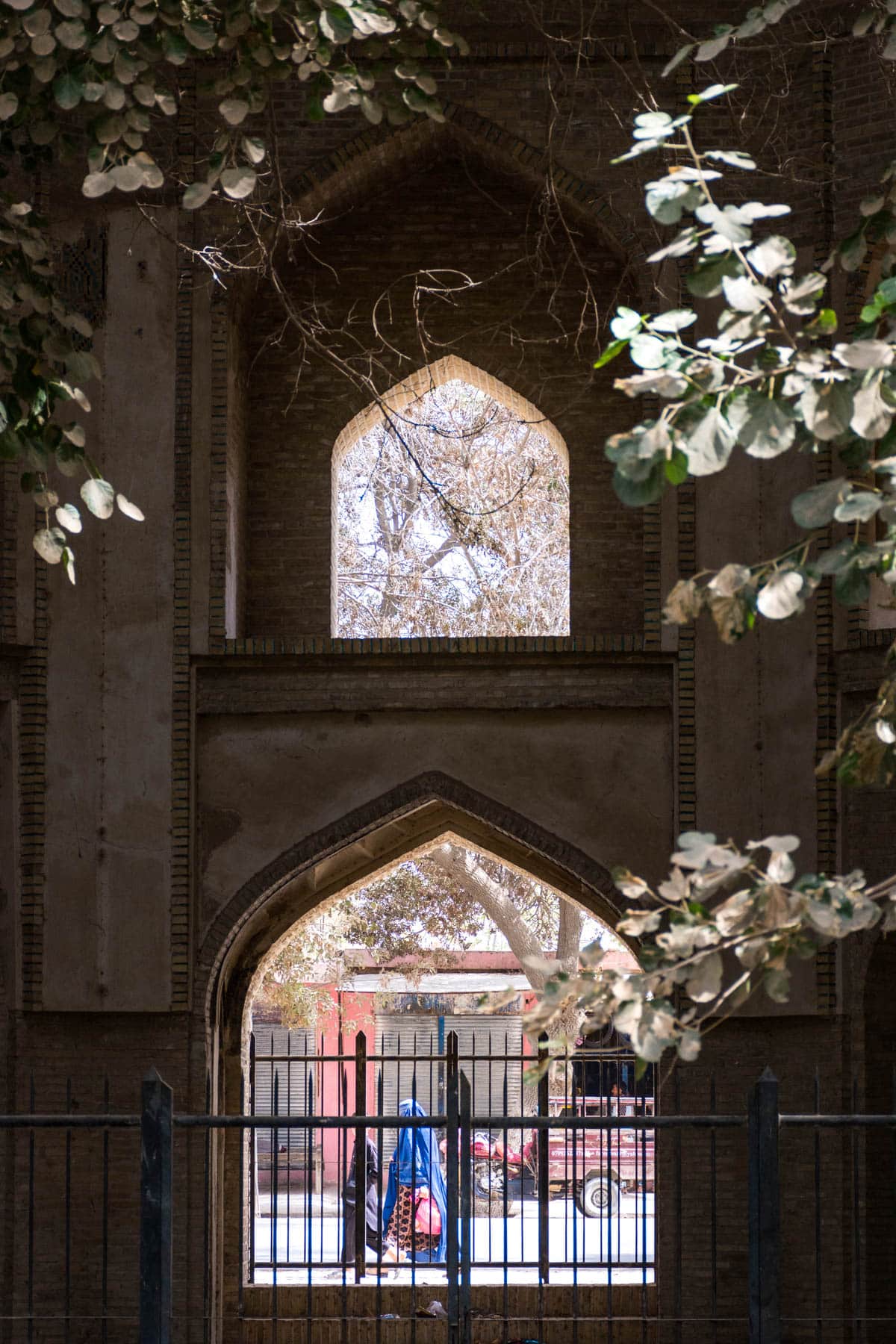 A woman in burqa walking past an abandoned mosque archway in Balkh, Afghanistan.