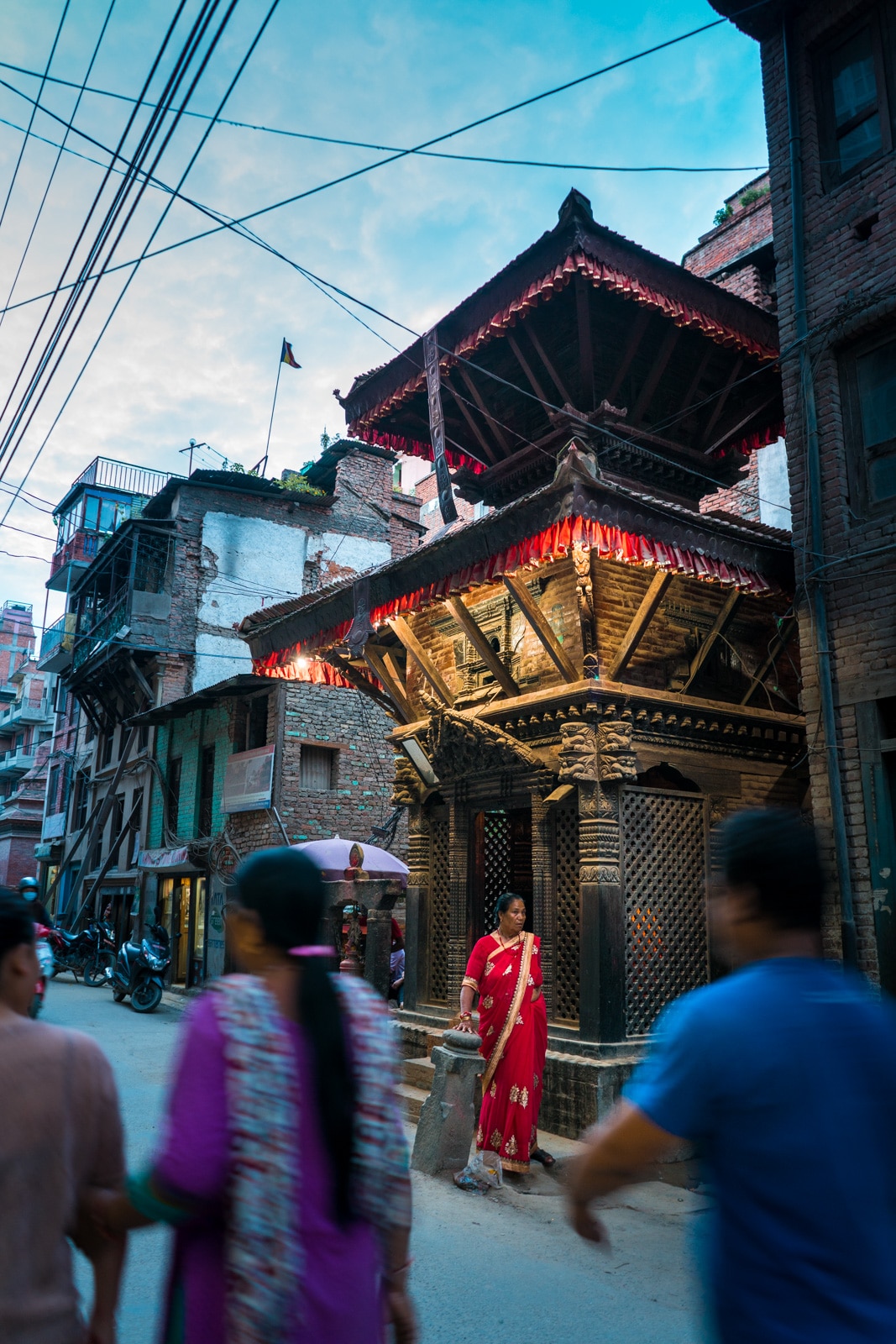 A local Nepali woman in a bright red sari before a small shrine on the busy streets of Patan, Nepal during twilight.