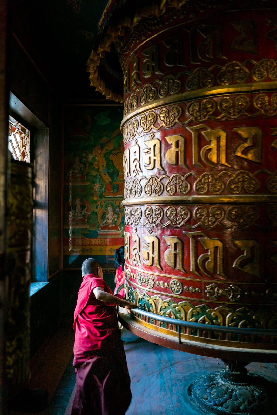 A young monk running around a Buddhist prayer wheel at Boudhanath stupa in Kathmandu, Nepal.