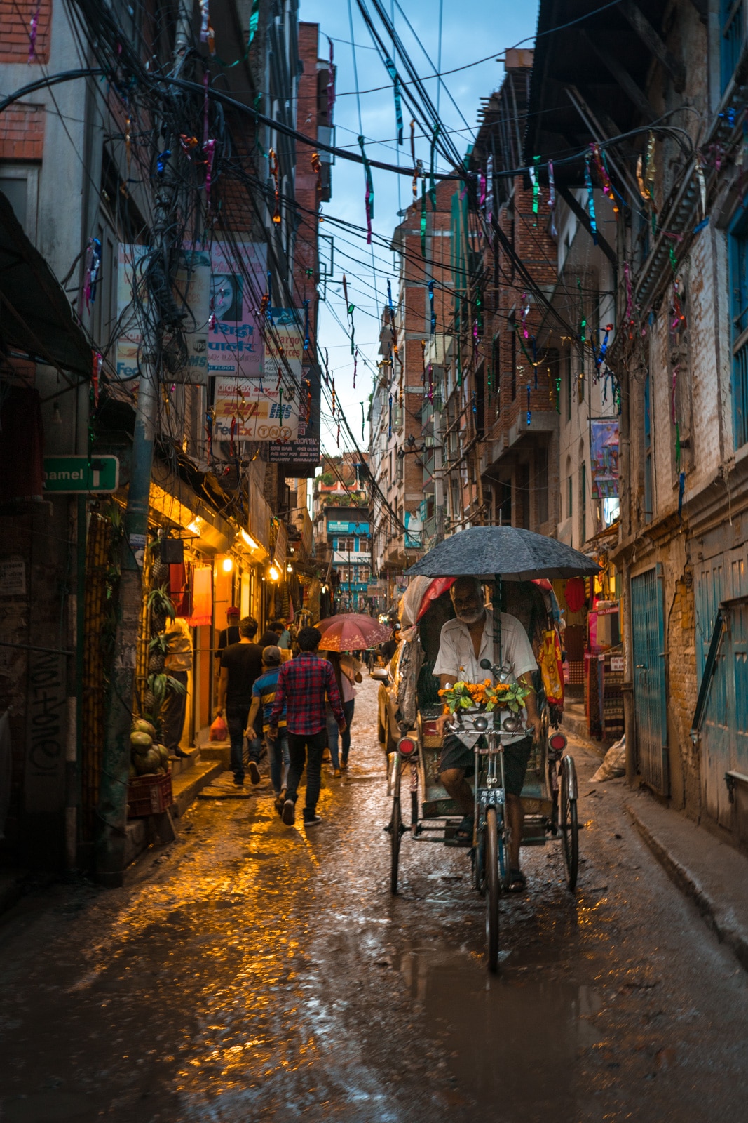 A cycle rickshaw driver cycling through the wet streets of Kathmandu, Nepal during monsoon.