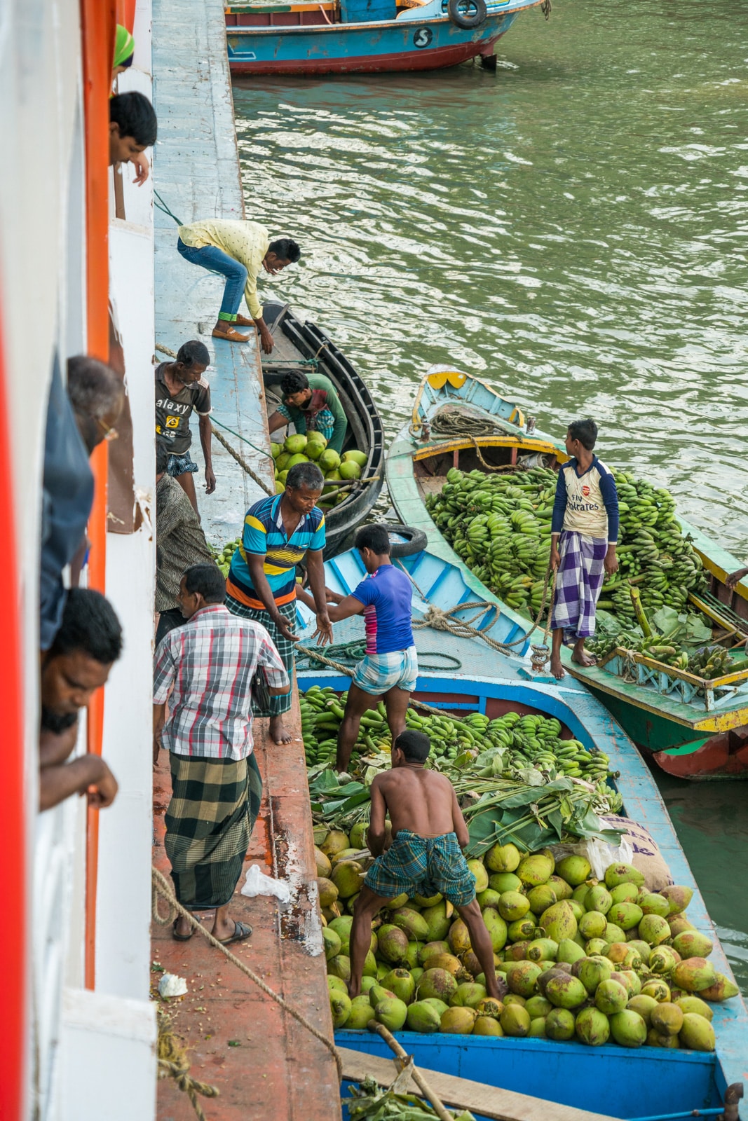 Several boats of men loading bananas and coconuts onto a launch boat in Bangladesh.