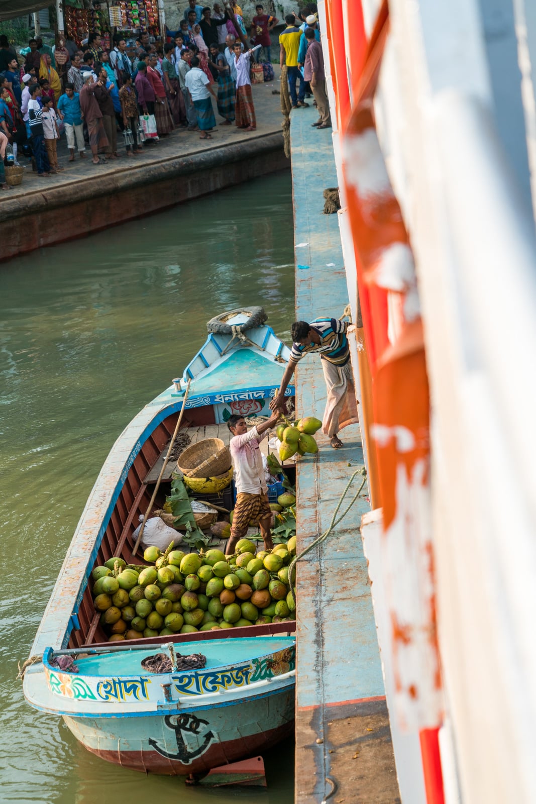 Men loading coconuts onto a launch ferry boat on the Kaliganga river in Bangladesh.