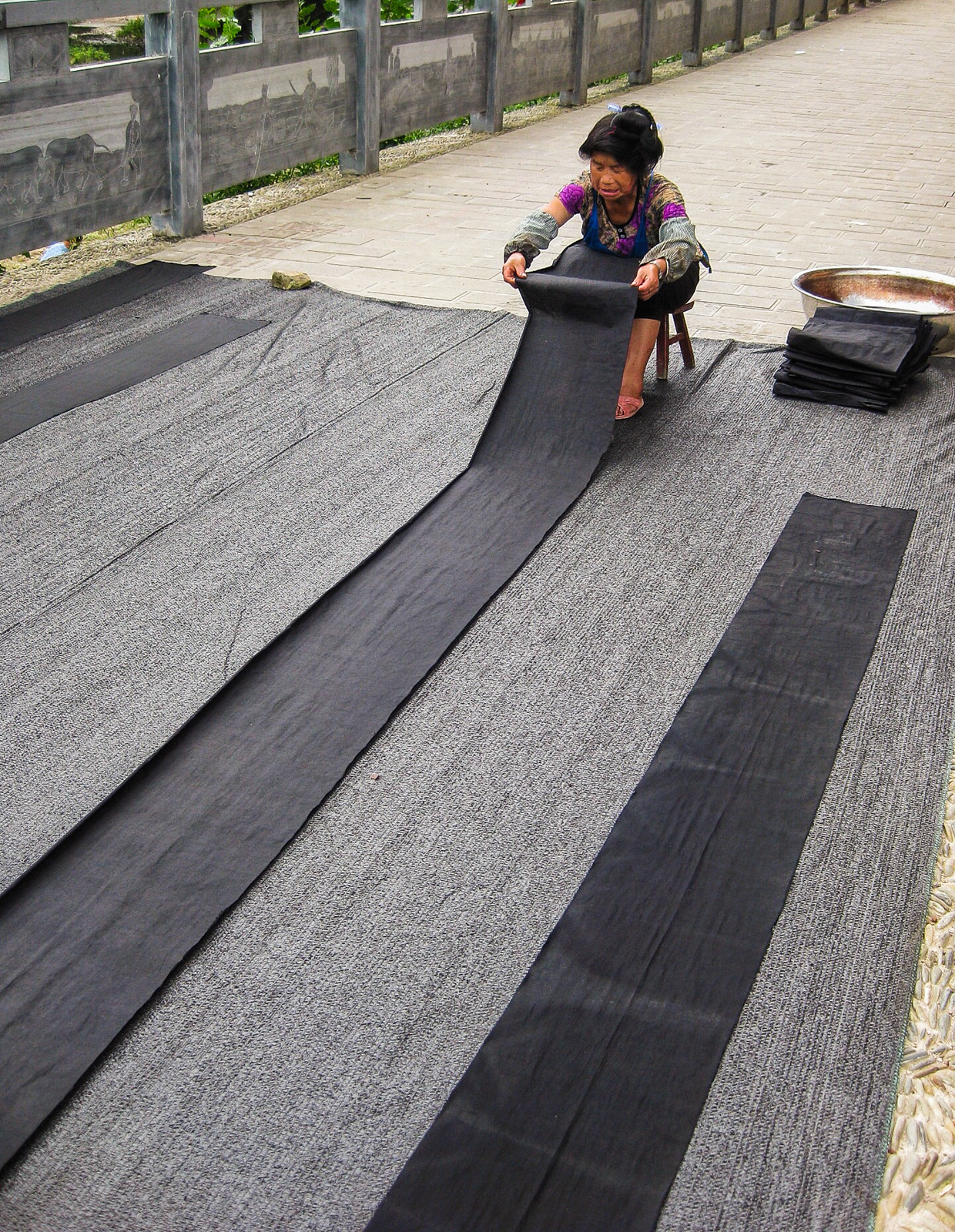 Exploring off the beaten track villages in Guizhou, China - Woman drying indigo dyed material in Zhouxi