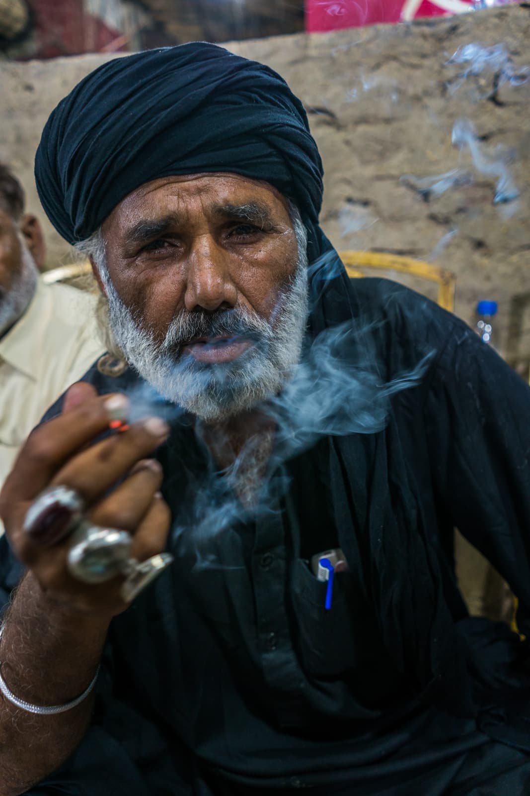 A Sufi melang in black smoking a cigarette at the Urs of Lal Shahbaz Qalandar in Sehwan Sharif, Pakistan.