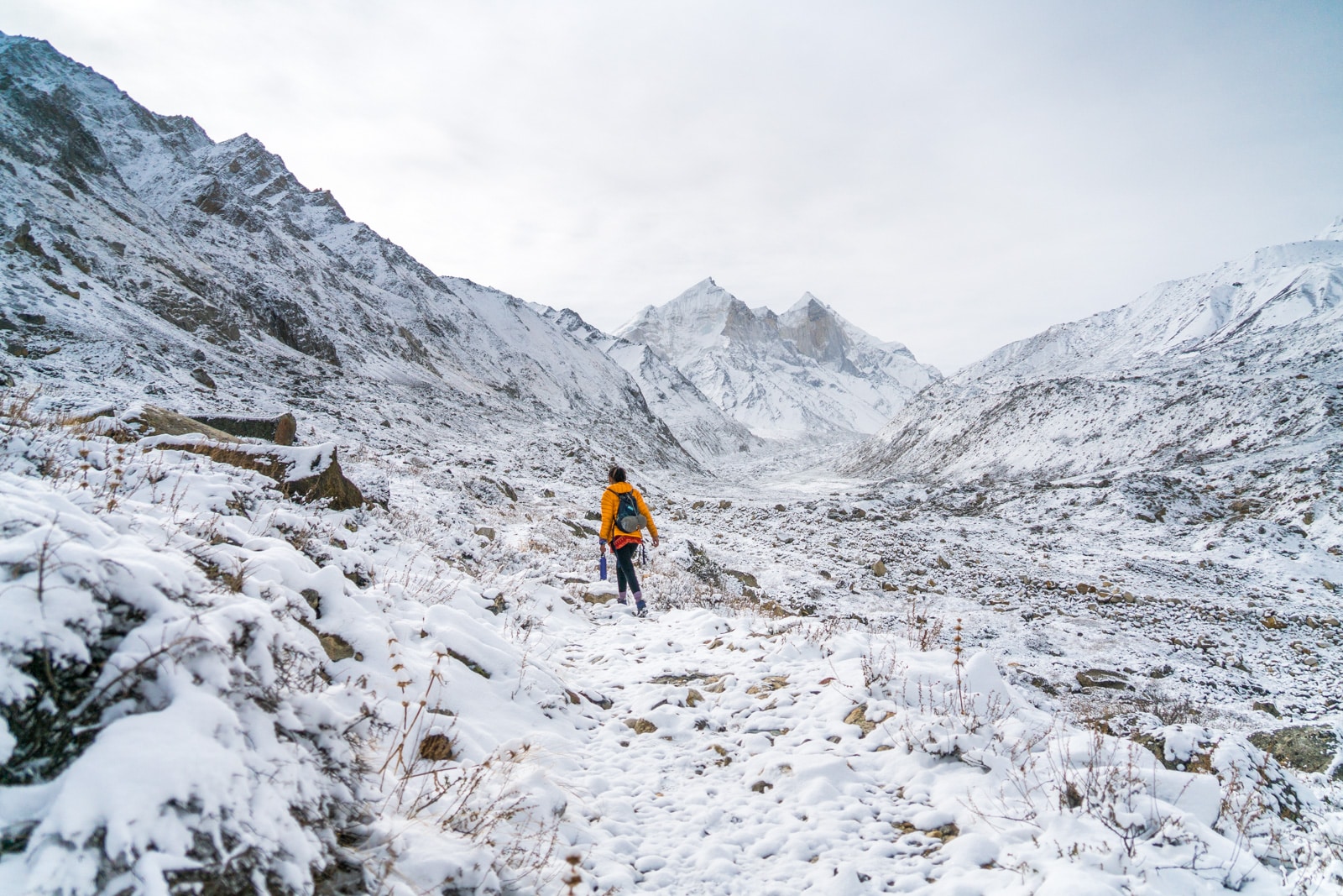 A girl walking in a yellow coat through snowy mountains