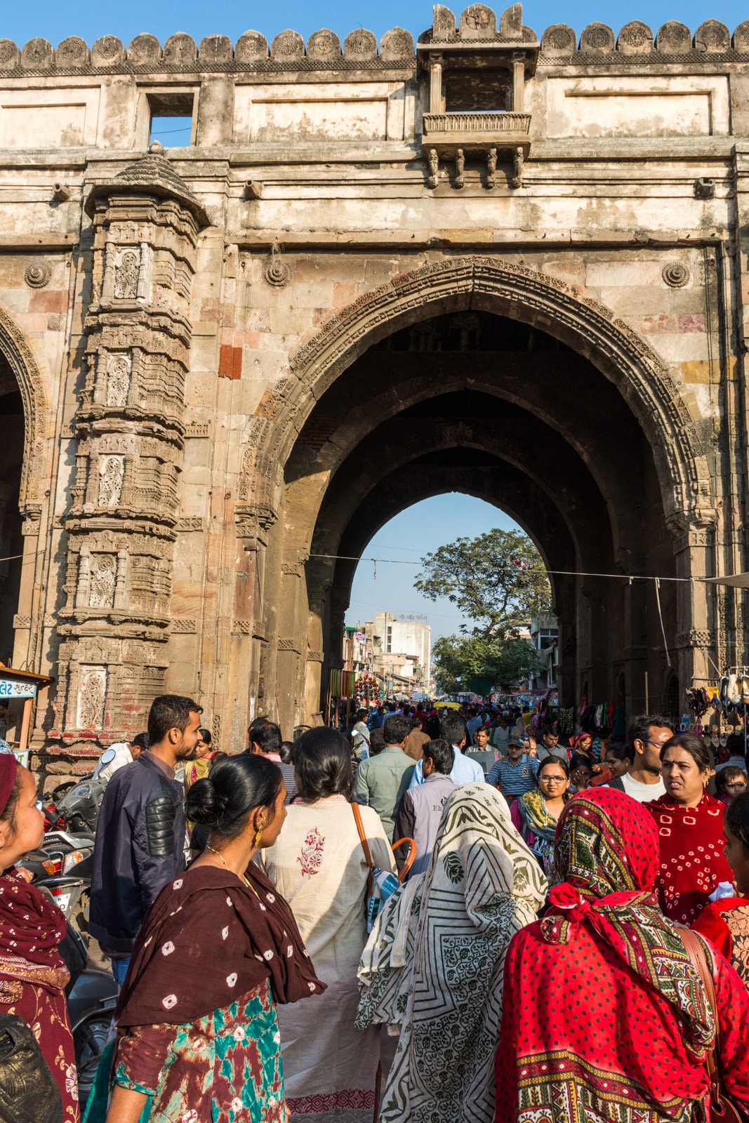 A busy crowd walks through an ornate stone archway over a market street in Ahmedabad