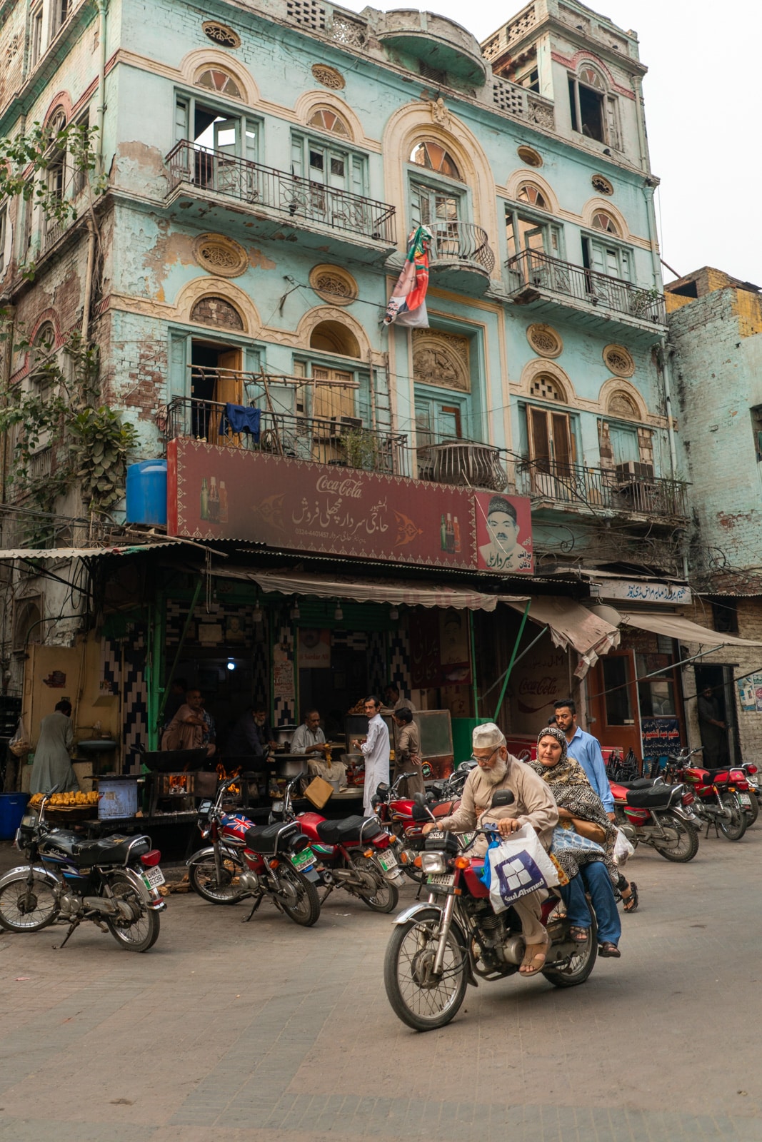 A couple driving a motorbike in front of a colorful building on Gawalmandi Food Street in Lahore, Pakistan