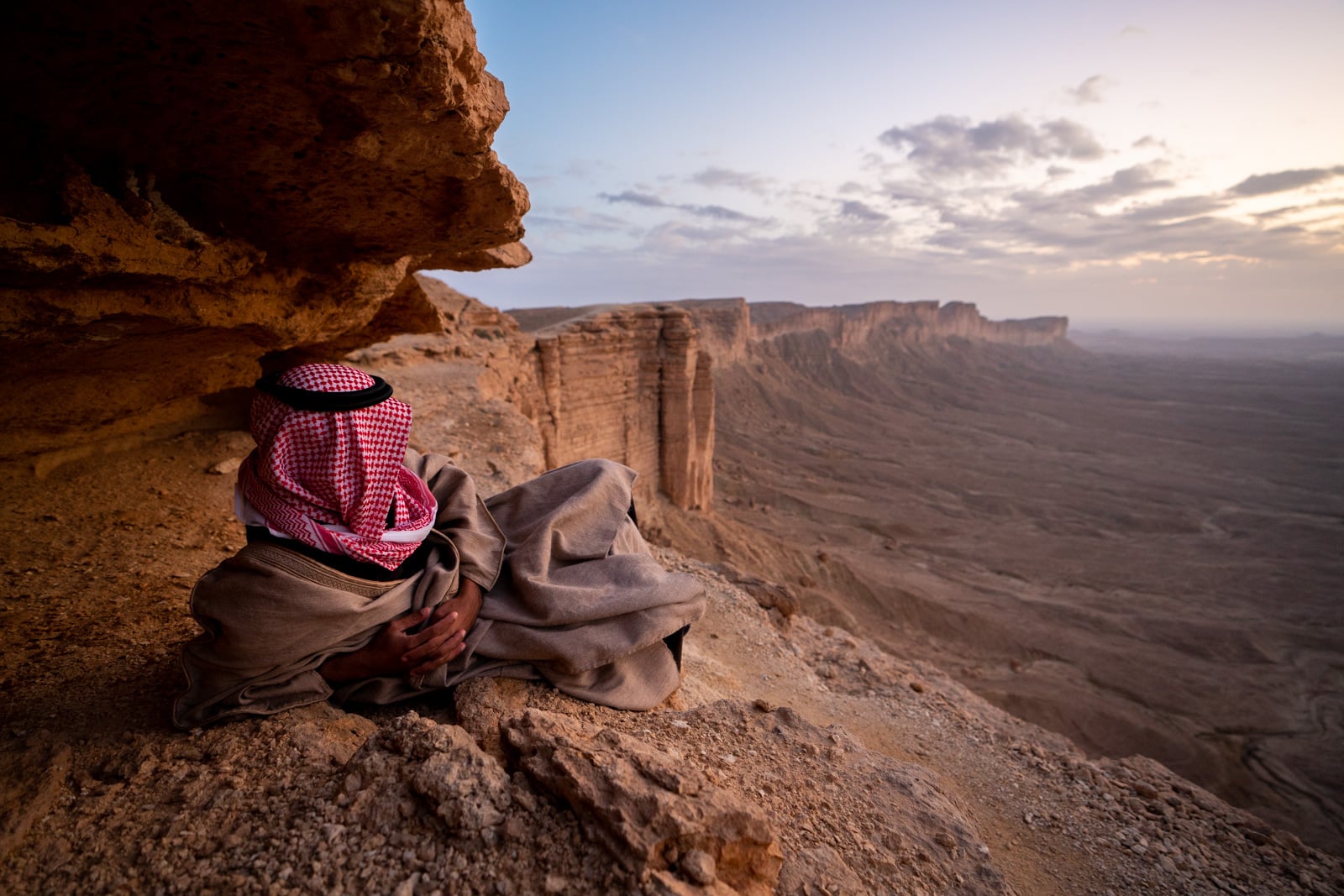 Saudi man sitting at the Edge of the World near Riyadh, Saudi Arabia, at sunset