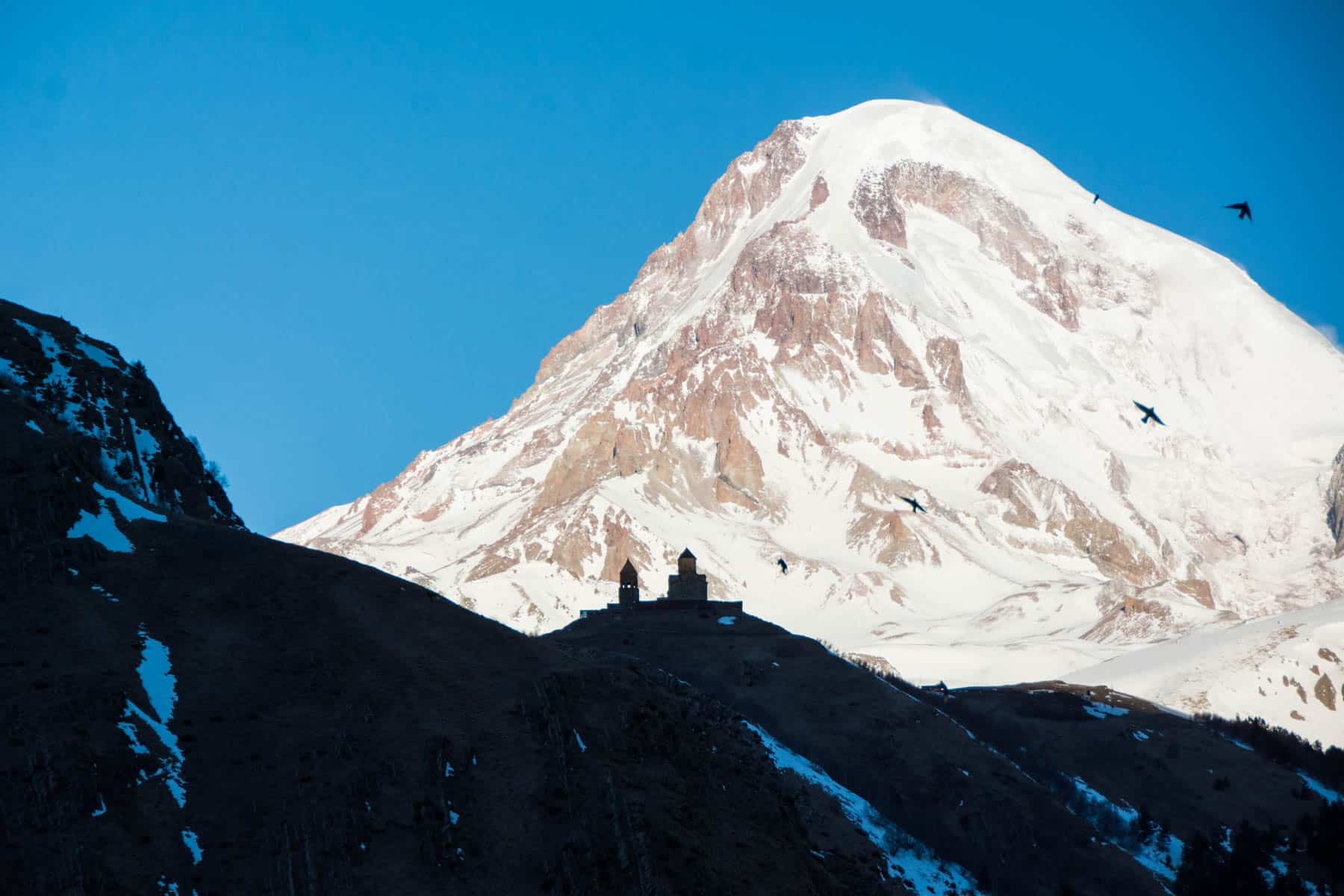 Birds flying over Gergeti Trinity Cathedral and Mount Kazbek in Stepantsminda, Georgia