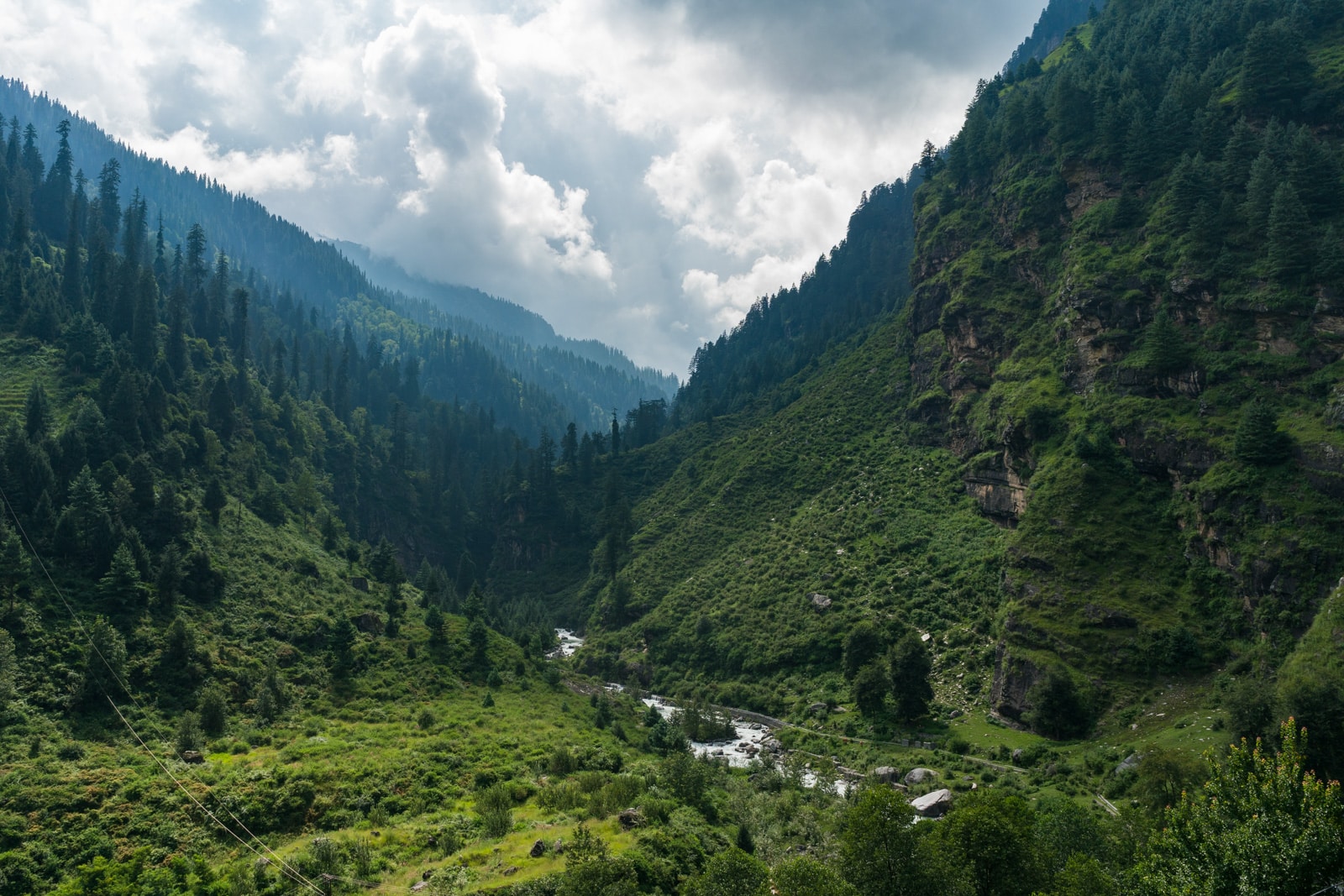 Green forested mountains with a small river running down a valley near Manali in Himachal Pradesh, India