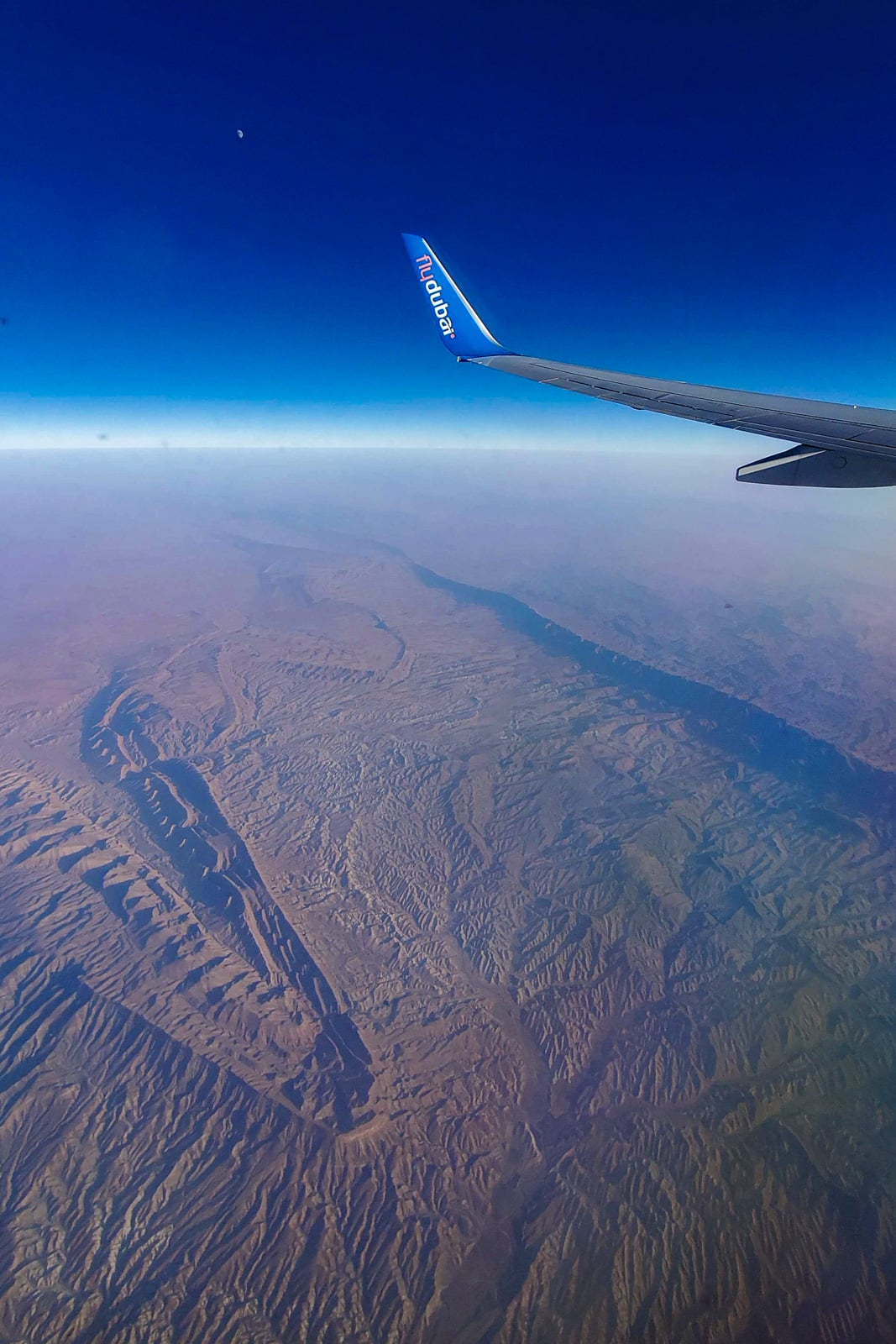 Fly Dubai plane wing flying over desert rock formations