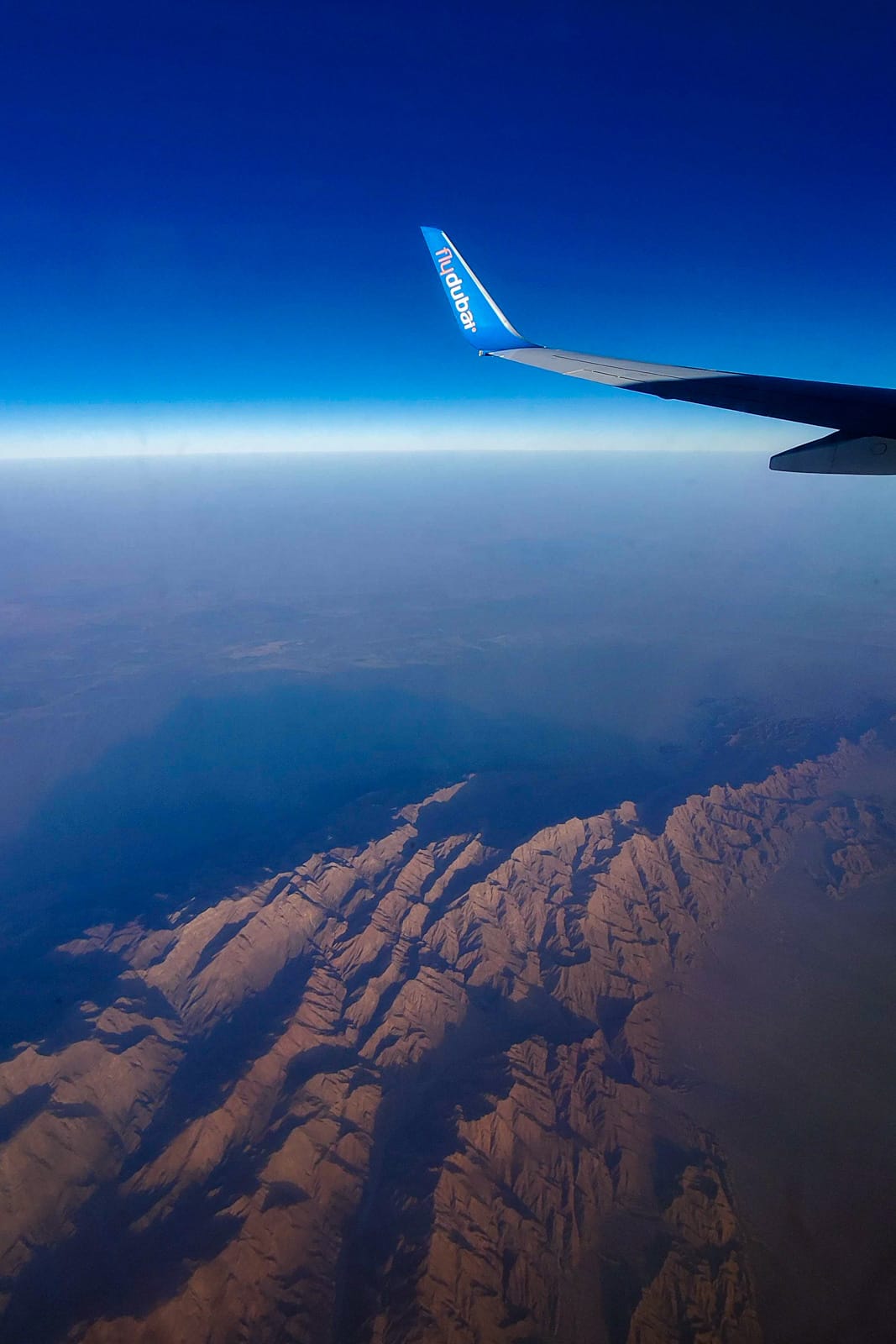 Fly Dubai plane wing flying over desert rock formations at sunset