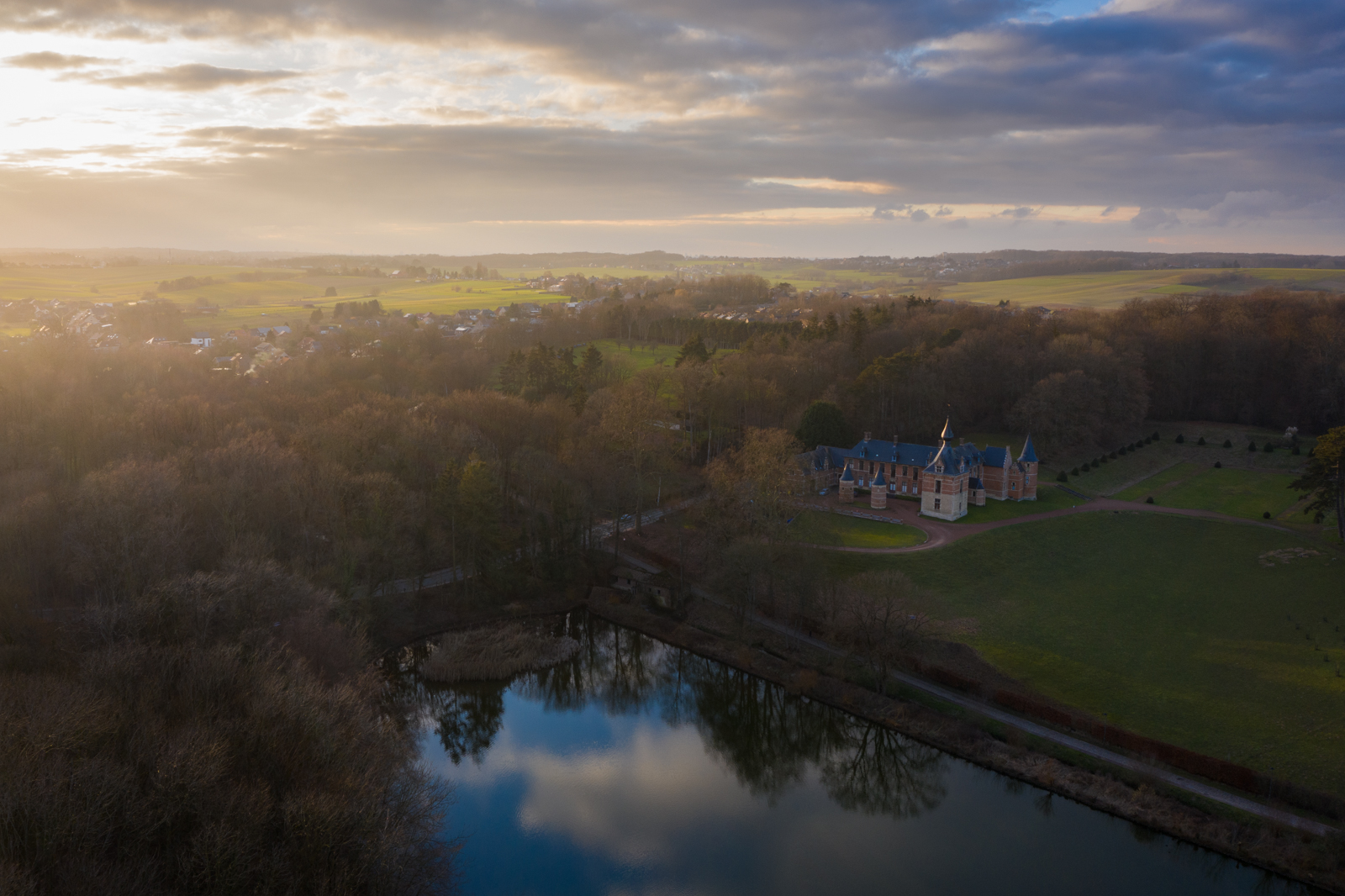 Leefdaal castle at sunrise as clouds reflect in the nearby lake