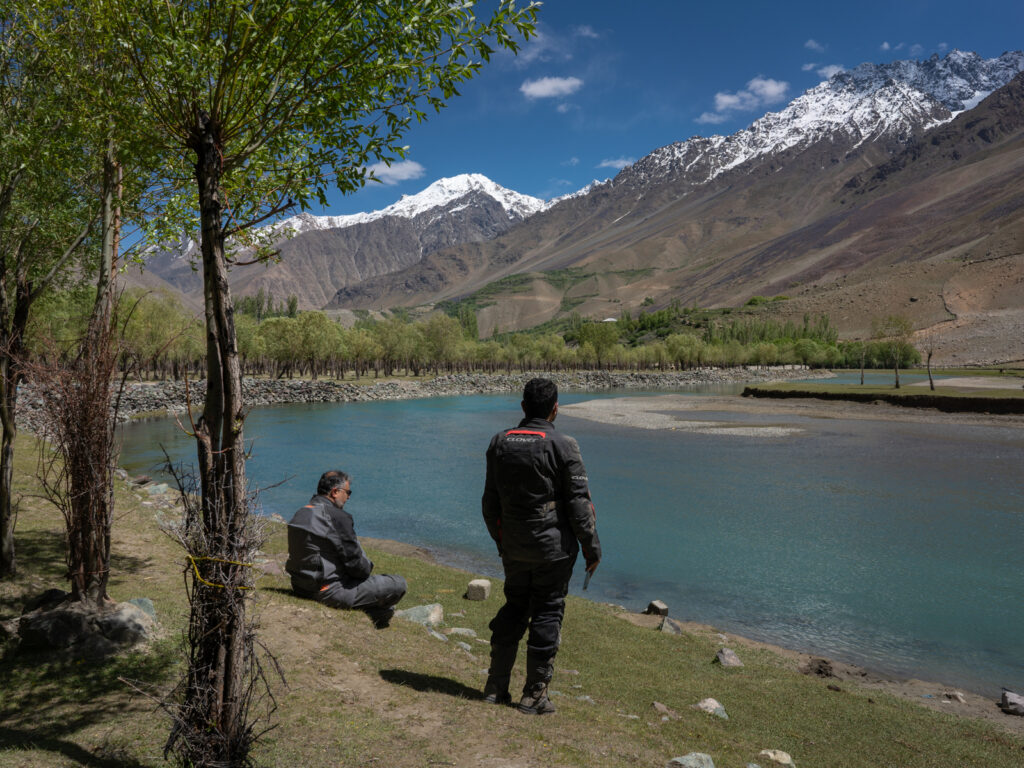 Bikers relaxing by the Gilgit River in Phander Valley while on a Pakistan adventure motorcycle tour