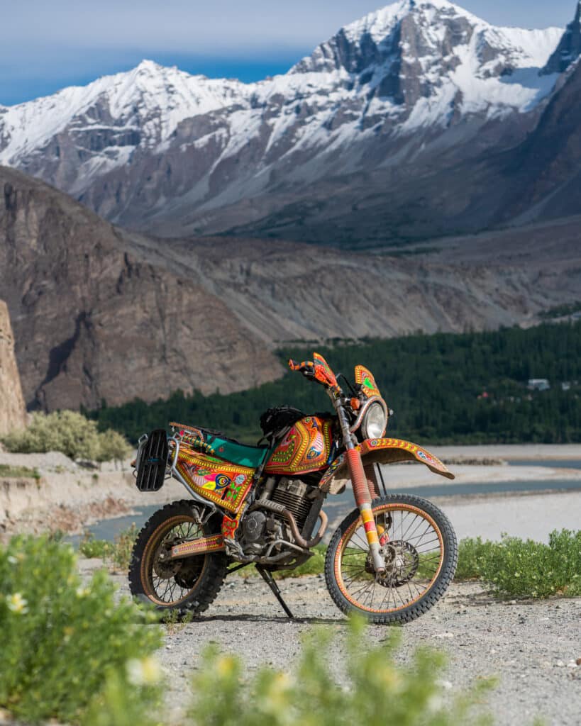 Truck art motorcycle rental in Pakistan, parked on the banks of the river near Khaplu