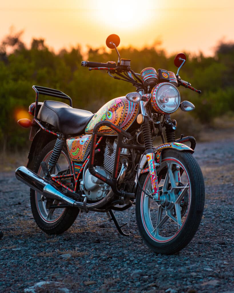 Suzuki GS 150 SE motorcycle covered in Pakistani truck art, during sunset in Islamabad