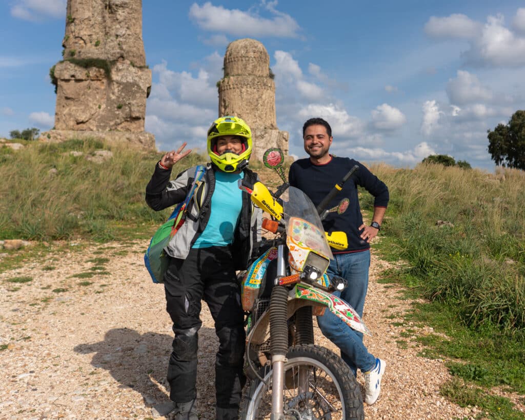 Alex and her guide, Rami, posing with motorcycle in front of phallic temple ruins in Amrit, Syria